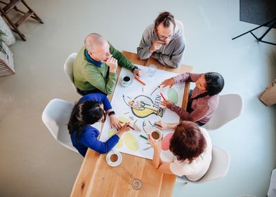 Fünf Personen arbeiten an einem Tisch an einer Collage zum Thema "Ideen"